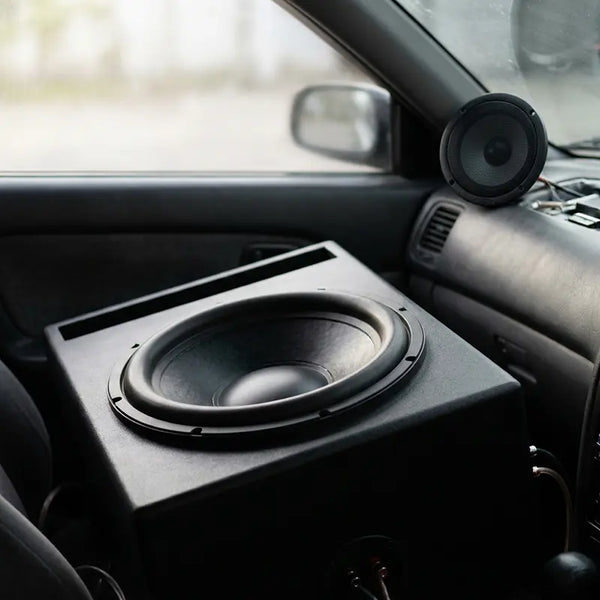 Großer Subwoofer im Vordergrund neben kleinem Frontlautsprecher am Armaturenbrett, unausgewogenes Setup